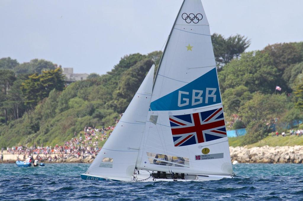 Iain Percy and Bart Simpson salute the crowd before the Medal Race of the 2012 Olympics. The gold start of the top of the mainsail is for a former world champion, the gold circle at the bottom is for the fleet leader in the Olympic event © Richard Gladwell www.photosport.co.nz